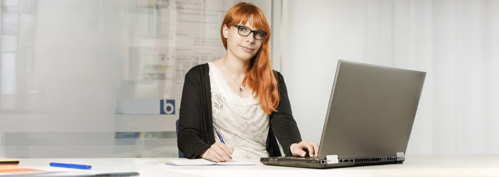Eine Frau mit langen roten Haaren schreibt am Laptop