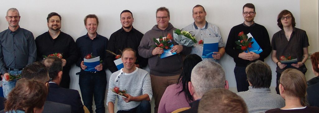 eine Gruppe Umschüler hält Zeugnisse und Blumen in der Hand