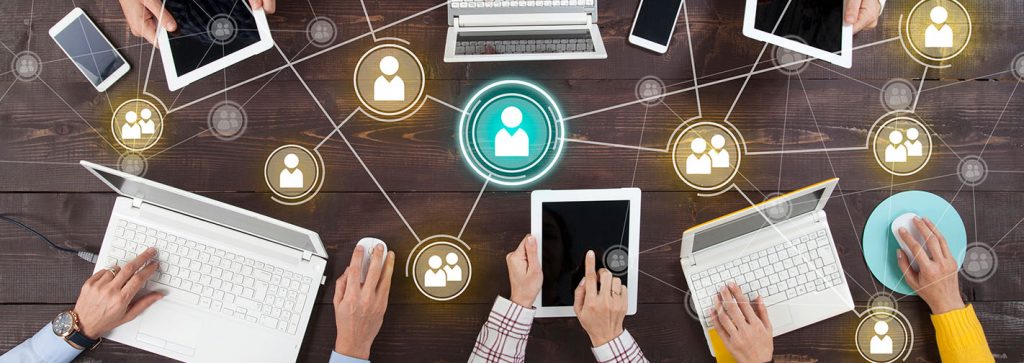 mehrere Personen arbeiten an einem großen Holztisch an Tablets und Laptops