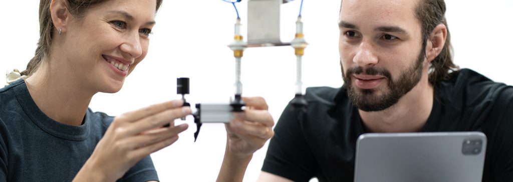 ein Mann und eine Frau vermessen ein Bauteil mit einem Messschieber