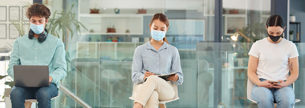 3 Personen mit Schutzmasken sitzen mit Abstand zueinander