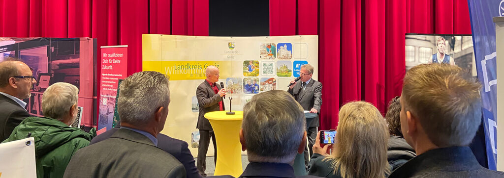 zwei Männer sprechen in Mikrofone auf einer Bühne