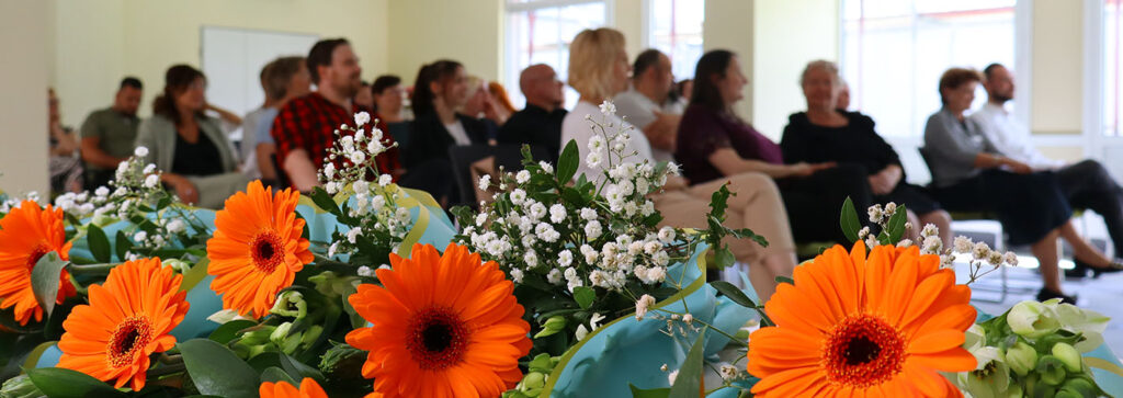 mehere Blumensträuße liegen auf einem Tisch. Dahinter sind verschwommen die Absolventen zu sehen.